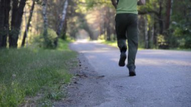 Asfalt yolda koşan sporcu. Kırsal şehir parkı. Yeşil ağaç ormanı ve ufukta güneş ışığı.
