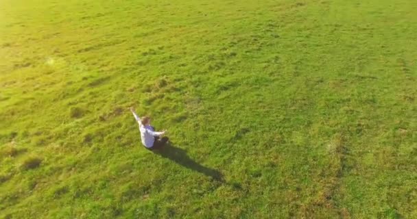 Vuelo orbital bajo alrededor del hombre sobre hierba verde con bloc de notas en el campo rural amarillo. — Vídeos de Stock