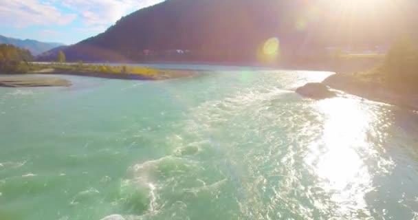 Vol à basse altitude au-dessus d'une rivière de montagne fraîche et rapide avec des rochers au soleil matin d'été. — Video