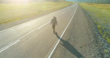 Asfalt yolda yürüyen otostopçu turist üzerinden uçuş. Yaz günü büyük bir kırsal vadi. Sırt çantalı gezgin..