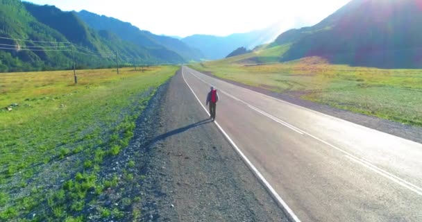 アスファルトの道路を歩くヒッチハイカーの観光客の上のフライト。夏の日に巨大な田舎の谷。リュックハイキング男. — ストック動画