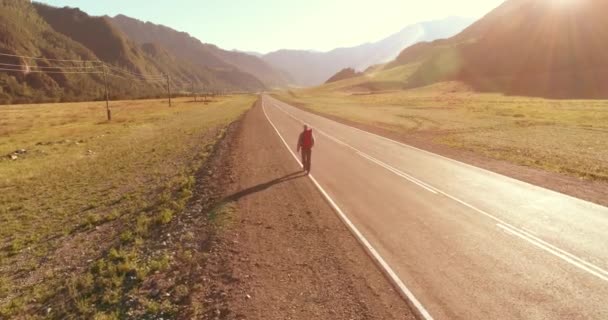 アスファルトの道路を歩くヒッチハイカーの観光客の上のフライト。夏の日に巨大な田舎の谷。リュックハイキング男. — ストック動画