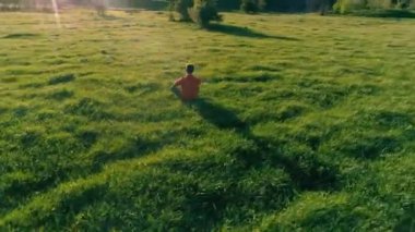 Yeşil çimlerde spor yogacısı üzerinde alçak irtifa radyal uçuş. Dağda gün batımı.