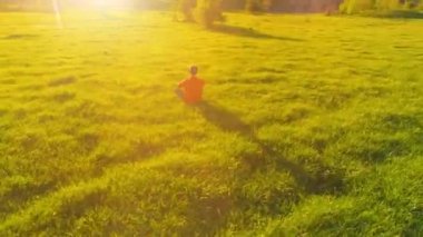 Yeşil çimlerde spor yogacısı üzerinde alçak irtifa radyal uçuş. Dağda gün batımı.