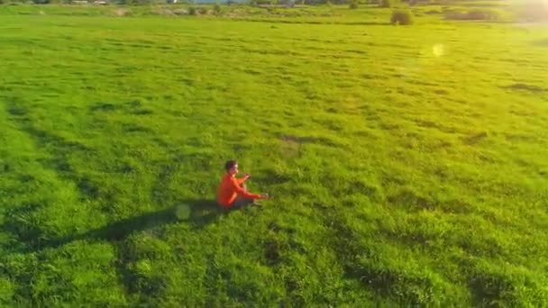 Vuelo radial de baja altitud sobre el hombre del yoga del deporte en hierba verde perfecta. Puesta de sol en montaña. — Vídeos de Stock