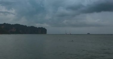 Kumsalda ve teknelerle deniz manzarasında yağmur bulutları hızlanıyor. Okyanusta tropik fırtına.