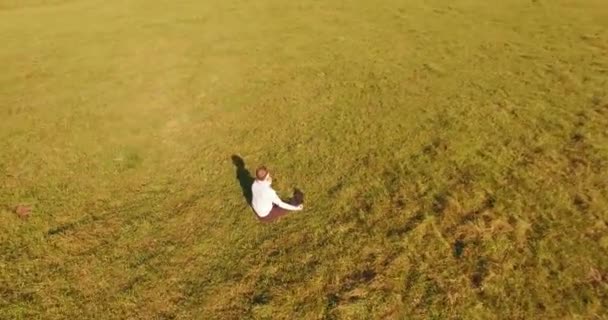 Vol orbital bas autour de l'homme sur herbe verte avec bloc-notes au champ rural jaune. — Video