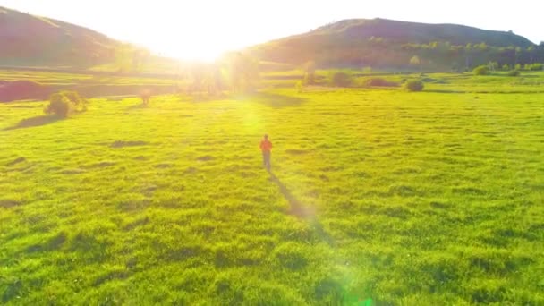 Voo sobre o homem do esporte no prado de grama verde perfeito. Pôr do sol na montanha — Vídeo de Stock