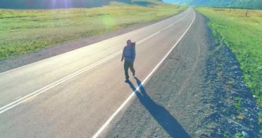 Asfalt yolda yürüyen otostopçu turist üzerinden uçuş. Yaz günü büyük bir kırsal vadi. Sırt çantalı gezgin..