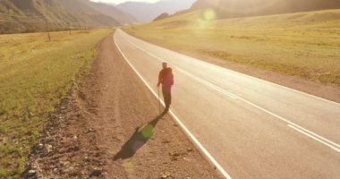 Asfalt yolda yürüyen otostopçu turist üzerinden uçuş. Yaz günü büyük bir kırsal vadi. Sırt çantalı gezgin..