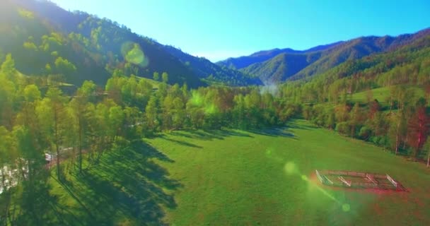 Mid air flight over fresh mountain river and meadow at sunny summer morning. Rural dirt road below. — Stock Video