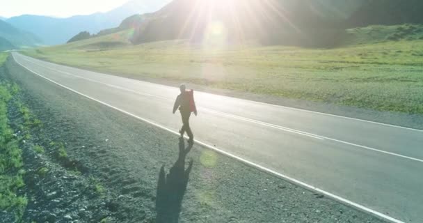 Vuelo sobre autoestopista turista caminando por carretera asfaltada. Gran valle rural en el día de verano. Mochila senderismo chico. — Vídeos de Stock