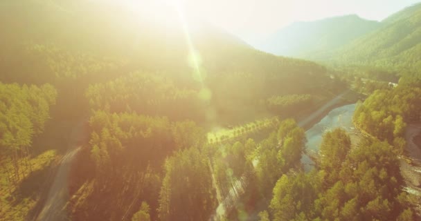 Mid air flight over fresh mountain river and meadow at sunny summer morning. Rural dirt road below. — Stock Video