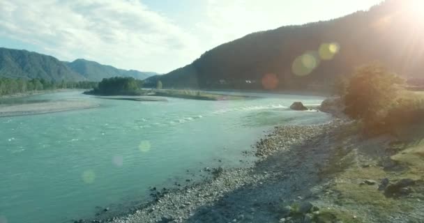 Vol à basse altitude au-dessus d'une rivière de montagne fraîche et rapide avec des rochers au soleil matin d'été. — Video