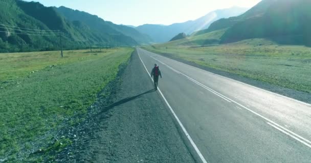 Flight over hitchhiker tourist walking on asphalt road. Huge rural valley at summer day. Backpack hiking guy. — Stock Video