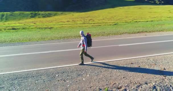 Flyg över liftare turist promenader på asfalterad väg. Enorm lantlig dal på sommardagen. Ryggsäck vandring kille. — Stockvideo