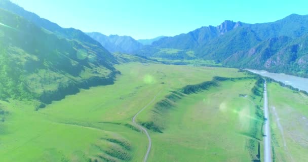 Luftlinie ländliche Bergstraße und Wiese an einem sonnigen Sommermorgen. Asphaltstraße und Fluss. — Stockvideo