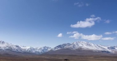 Güneş 'in kristal berrak gökyüzünde, kar dağının tepesindeki bulutlarla hareket zamanı. Sonbahar yüksek rakımlı çayırlarda sarı çimenler. Vahşi sonsuz doğa..