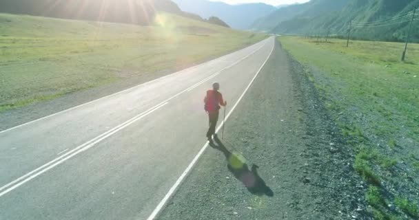 Volo sopra autostoppista turistico a piedi su strada asfaltata. Enorme valle rurale durante la giornata estiva. Zaino escursionista ragazzo. — Video Stock