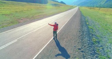 Asfalt yolda yürüyen otostopçu turist üzerinden uçuş. Yaz günü büyük bir kırsal vadi. Sırt çantalı gezgin..