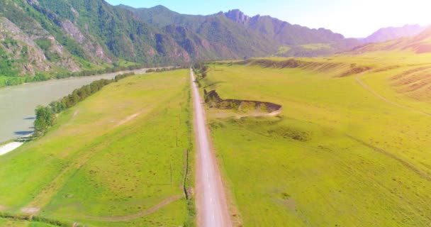 Luftlinie ländliche Bergstraße und Wiese an einem sonnigen Sommermorgen. Asphaltstraße und Fluss. — Stockvideo