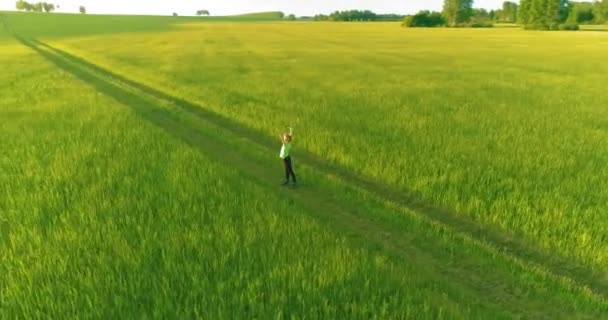Sportowe dziecko stojące na zielonym polu pszenicy z podniesionymi rękami w górze. Wieczorne ćwiczenia sportowe na wiejskiej łące. Szczęśliwe dzieciństwo to zdrowy styl życia. Radialny ruch panoramiczny, promienie słoneczne i — Wideo stockowe