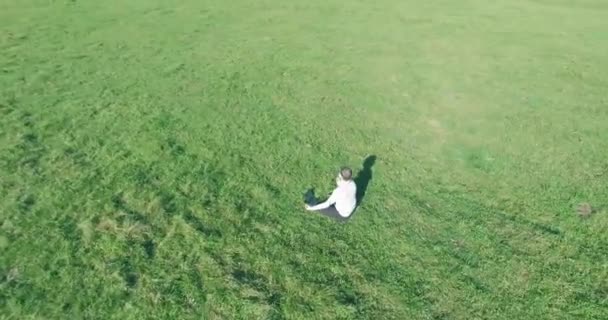 Vol orbital bas autour de l'homme sur herbe verte avec bloc-notes au champ rural jaune. — Video