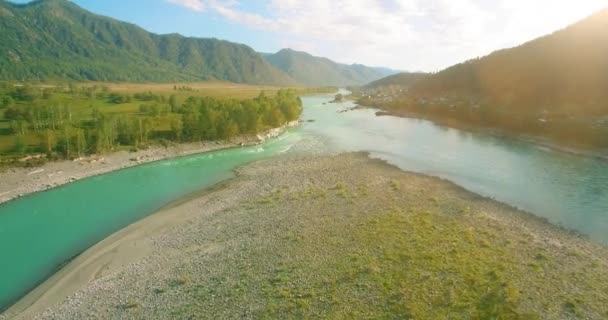 Vol à basse altitude au-dessus d'une rivière de montagne fraîche et rapide avec des rochers au soleil matin d'été. — Video