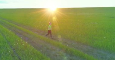 Sportif çocuk yeşil buğday tarlasında koşuyor. Kırsal çayırlarda akşam sporu alıştırmaları. Mutlu bir çocukluk sağlıklı bir yaşam biçimidir. Radikal hareket, güneş ışınları ve ot.
