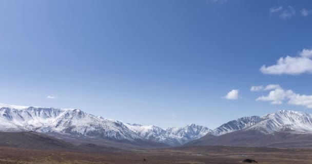 太阳在晶莹明亮的天空中移动的时间，雪山顶上布满了云彩。秋天的高原地区黄草丛生.野生无穷无尽的自然. — 图库视频影像