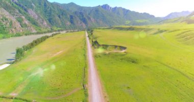 Güneşli yaz sabahında havadan kırsal dağ yolu ve çayır. Asfalt karayolu ve nehir.