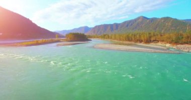 4k UHD hava görüntüsü. Güneşli yaz sabahında taze soğuk dağ nehri üzerinde alçak uçuş. Horisont 'ta yeşil ağaçlar ve güneş ışınları