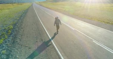 Asfalt yolda yürüyen otostopçu turist üzerinden uçuş. Yaz günü büyük bir kırsal vadi. Sırt çantalı gezgin..