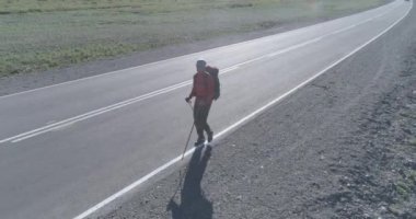 Asfalt yolda yürüyen otostopçu turist üzerinden uçuş. Yaz günü büyük bir kırsal vadi. Sırt çantalı gezgin..