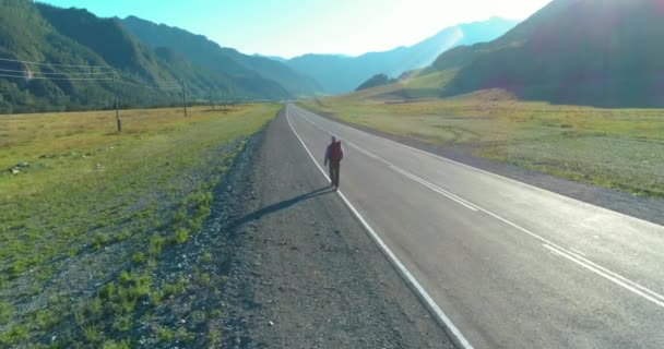 Vlucht over lifter toerist wandelen op asfalt weg. Enorme landelijke vallei op zomerdag. Rugzakwandelaar. — Stockvideo