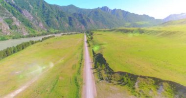 Güneşli yaz sabahında havadan kırsal dağ yolu ve çayır. Asfalt karayolu ve nehir.