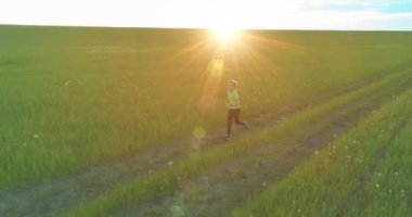 Sportif çocuk yeşil buğday tarlasında koşuyor. Kırsal çayırlarda akşam sporu alıştırmaları. Mutlu bir çocukluk sağlıklı bir yaşam biçimidir. Radikal hareket, güneş ışınları ve ot.