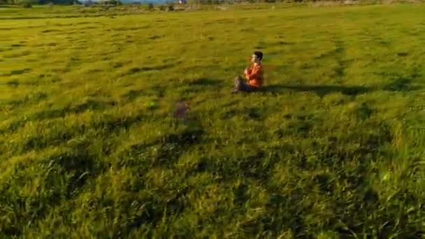 Vuelo radial de baja altitud sobre el hombre del yoga del deporte en hierba verde perfecta. Puesta de sol en montaña. — Vídeo de stock