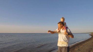 Baba ile kızı omuzlarında batımında sahilde yürüyüş