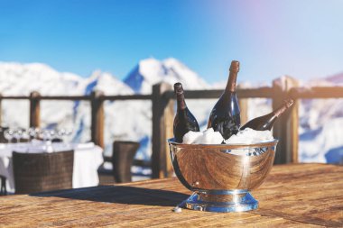 bucket with champagne bottles on restaurant table against snowy mountain background clipart