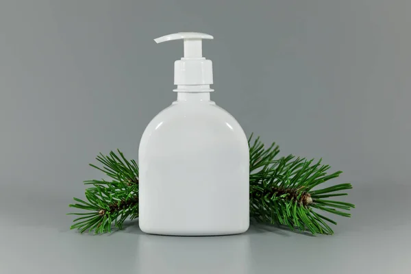 灰色の背景に松の木の枝を持つ白い空の香水ディスペンサーボトル — ストック写真