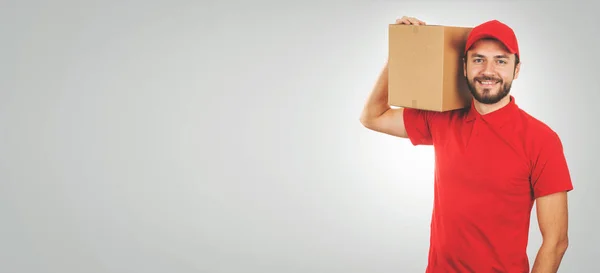 Молодой улыбающийся курьер в красной униформе и с коробкой отгрузки — стоковое фото