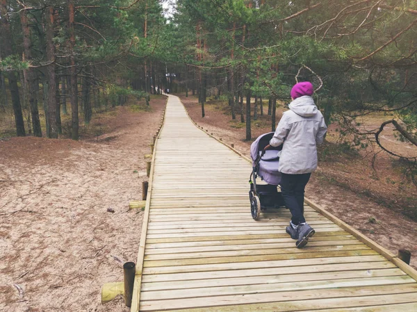 Vrouw met de kinderwagen lopen op houten voetpad in bos — Stockfoto