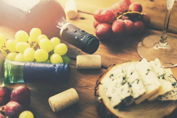 Garrafas de vinho uvas e queijo na velha mesa de madeira — Fotografia de Stock
