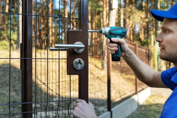 Trabajador que instala la cerradura para nuevas puertas de valla de metal — Foto de Stock