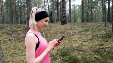 Genç sporcu kadın ormanda çalıştıktan sonra akıllı telefon kullanıyor.