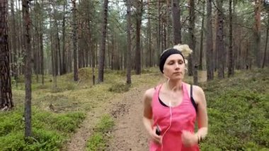 Genç bir kadın ormanda koşuyor ve akıllı telefondan müzik dinliyor.