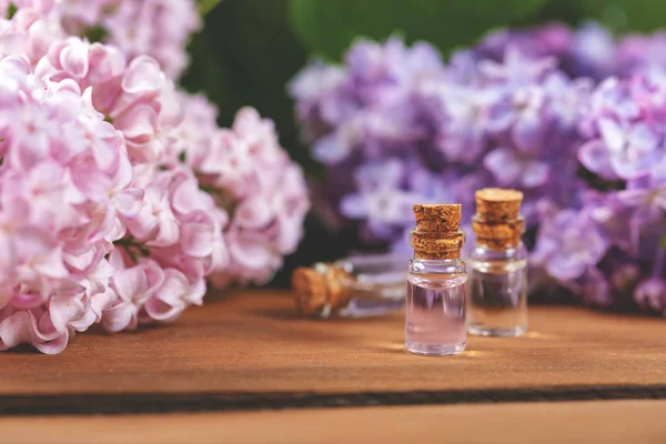 Garrafas de óleo essencial e flores lilás na mesa de madeira — Fotografia de Stock