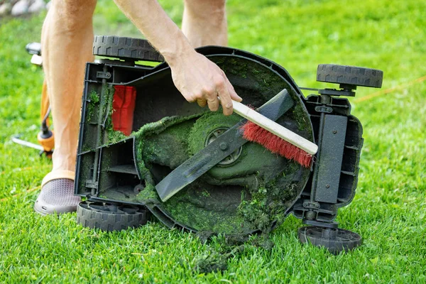 Mann mit Bürste reinigt Rasenmäher von altem Gras — Stockfoto