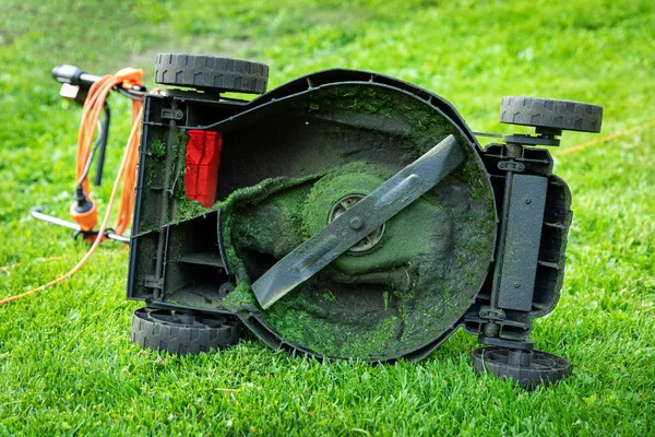 Грязная электрическая газонокосилка в зеленой траве на заднем дворе — стоковое фото
